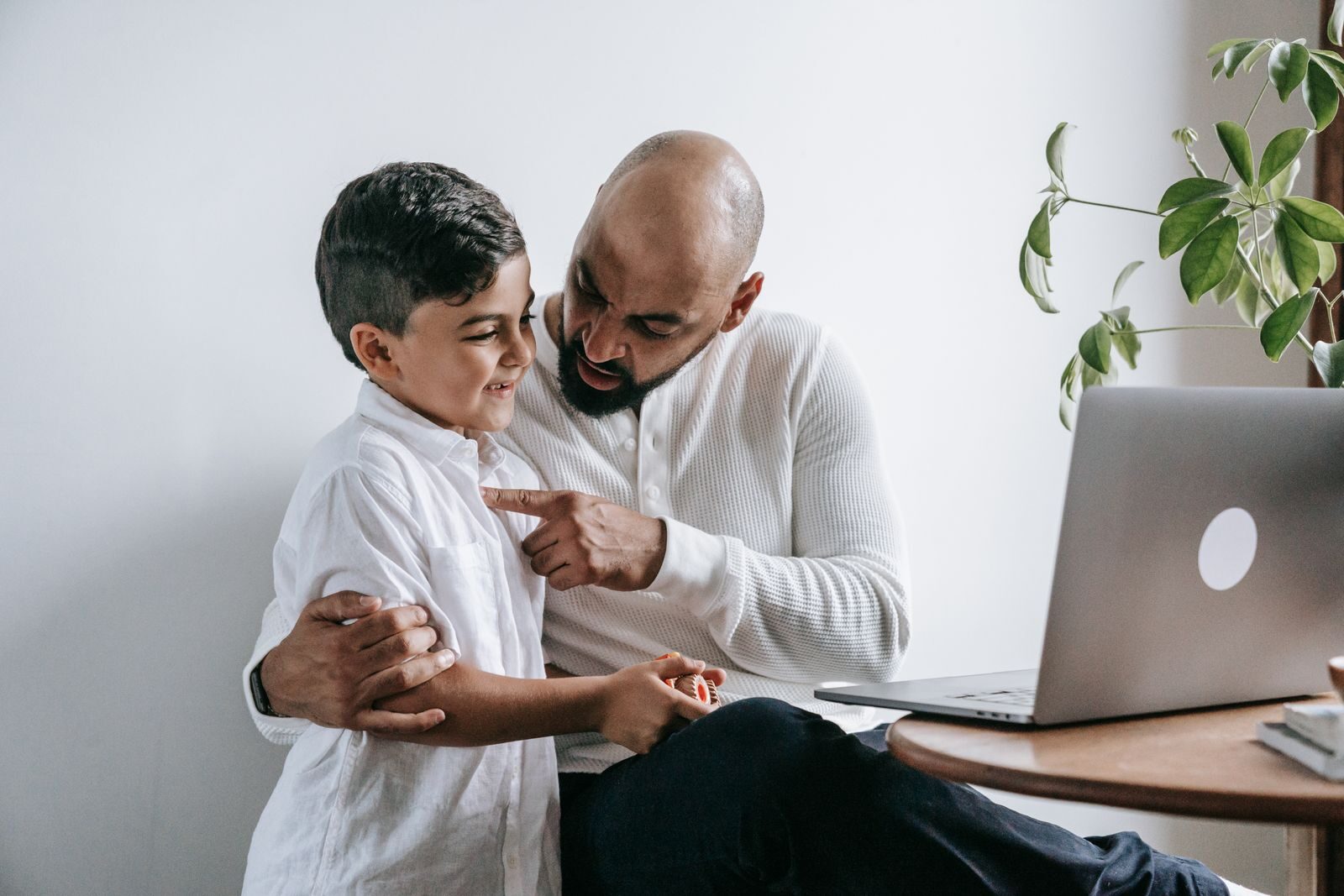 Heartwarming moment of a father and son interacting at home, with a laptop on the table.